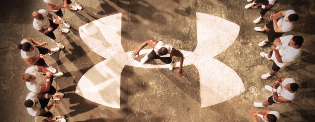 Under Armour logo shown on ground with men standing around it in a circle